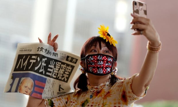 Một phụ nữ Nhật Bản chụp ảnh selfie với tờ báo đưa tin chiến thắng của Biden. (Ảnh: The Guardian)