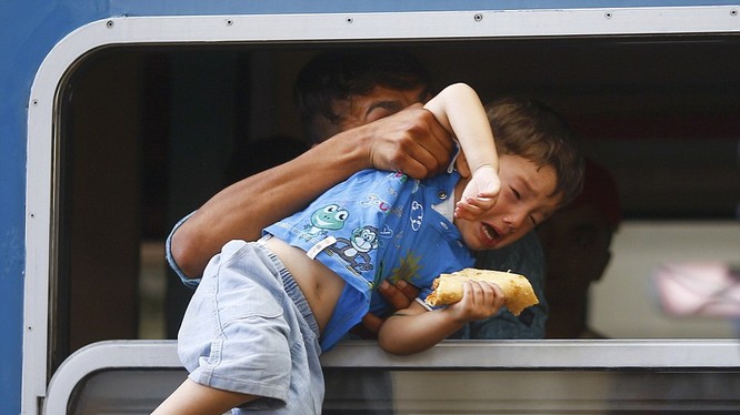 Một chú bé đang được cố kéo qua cửa sổ để lên con tàu chật ních những người chạy nạn đói khát và tuyệt vọng