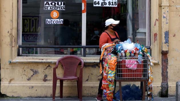 Một người phụ nữ đi ngang qua một tấm biển có nội dung “Bitcoin được chấp nhận ở đây”. Bitcoin đã được chấp nhận làm phương tiện thanh toán ở El Salvador từ ngày 7/9