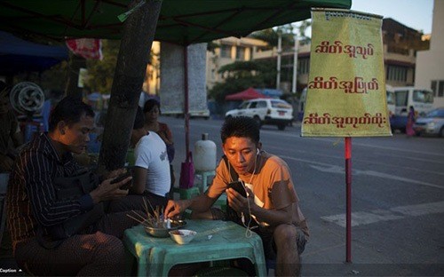 Sóng Viettel sắp chính thức phủ lên đất Myanmar. Trong ảnh là một người đàn ông Myanmar sử dụng điện thoại di động khi đang ngồi quán vỉa hè ở Yangon - Ảnh: Bloomberg.