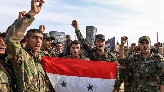 Quân đội chính phủ Syria giơ cao quốc kỳ và ảnh Tổng thống Assad tại ngoại ô thành phố Manbij hôm 15/10 (Ảnh: Newsweek)
