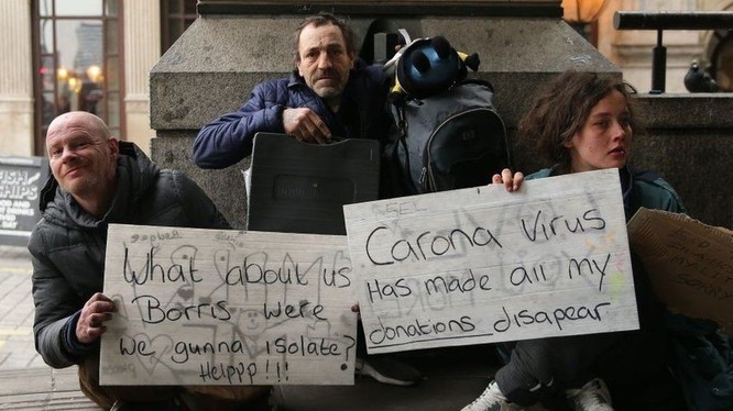 Người vô gia cư tại Luân Đôn (Anh) đang cầm tấm bảng với các thông điệp “Chúng tôi thì sao, Boris (Thủ tướng Anh)? Chúng tôi sẽ được cách ly chứ? Làm ơn giúp!”, “Virus Corona làm biến mất mọi thu nhập của tôi” - Ảnh: BBC.