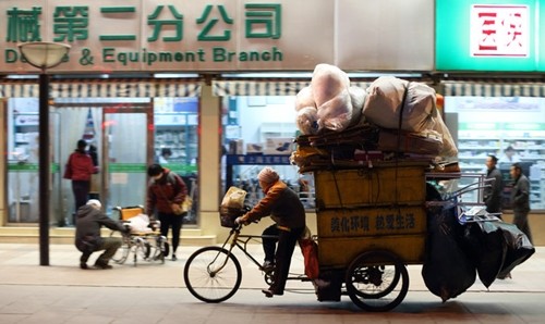 Một người đàn ông đang đạp xe qua một khu phố mua sắm tại Bắc Kinh. Ảnh:Bloomberg