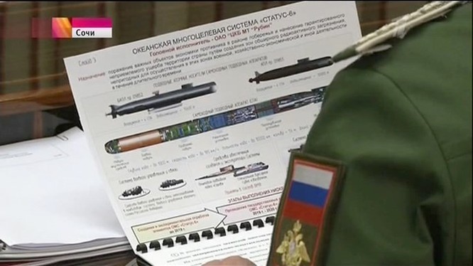 Hình ảnh tướng Andrei Kartapolov cầm tài liệu in rõ hệ thống vũ khí hải quân Status 6 của Nga đang được lan truyền trên mạng. Phía trên bên trái là tàu ngầm hạt nhân lớp 09852 mang dưới bụng 1 tàu ngầm không người lái, bên phải là tàu ngầm hạt nhân lớp 09