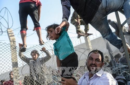 Người tị nạn Syria vượt qua hàng rào dây thép gai tại biên giới Thổ Nhĩ Kỳ ở Akcakale, tỉnh Sanliurfa. Ảnh: AFP/TTXVN