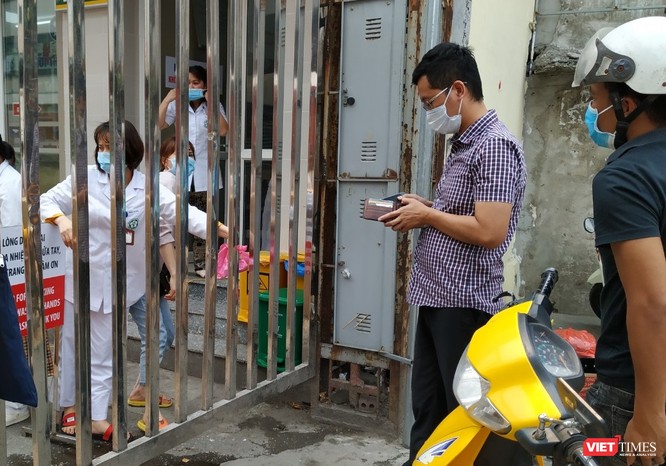 Người đàn ông áo kẻ lấy tiền để nhận số thuốc đựng trong nilon hồng từ tay nhân viên nhà thuốc tại cổng Bạch Mai trên phố Phương Mai.