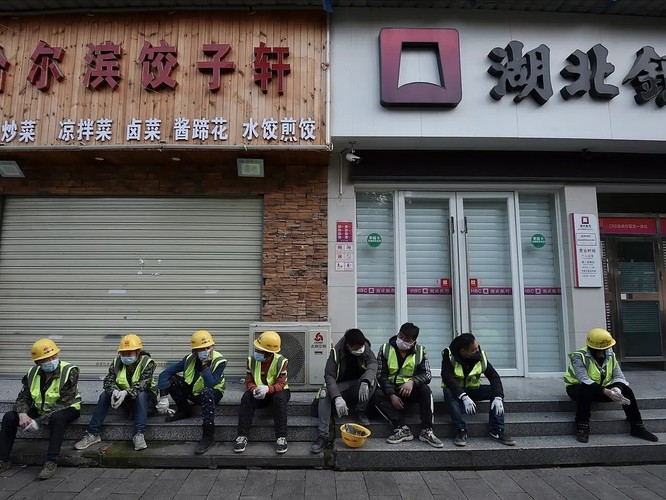 Công nhân ngồi bên ngoài một nhà hàng đã đóng cửa ở Vũ Hán, Trung Quốc ngày 23/2. Ảnh: AP