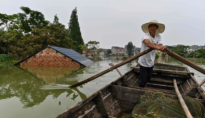 Một ngư dân lái thuyền qua một ngôi nhà bị nước phủ tới tận nóc ở Long Khẩu, Bà Dương, Giang Tây (Ảnh: AFP)