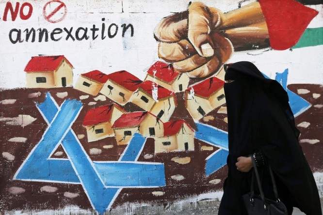 Một phụ nữ Palestine đi qua bức tranh cổ động chống kế hoạch sát nhập nhiều phần khu Bờ Tây của Israel (Ảnh: Reuters)