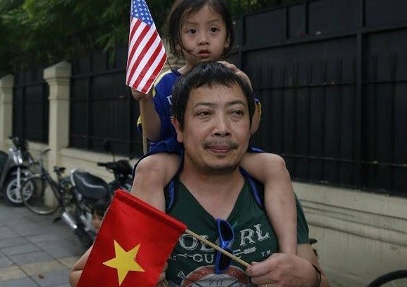 Em bé cầm cờ Mỹ và Việt Nam được bố đưa đi đón đoàn của tổng thống Obama. Trong khi đó, người dân đã dừng trên cầu vượt Kim Mã chờ đoàn xe tổng thống Mỹ qua.