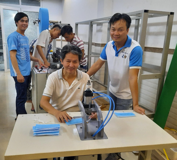 PGS.TS Nguyễn Hữu Lộc (ngồi) thử máy hàn quai siêu âm đơn điểm, bên máy tạo thân khẩu trang y tế (Ảnh- T.H )