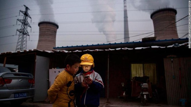Hai cậu bé xem điện thoại di động gần một nhà máy điện than ở ngoại ô thủ đô Bắc Kinh (Ảnh: CNN)