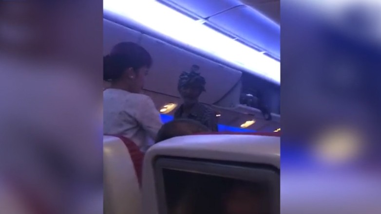 Một người đàn ông cầm túi nhựa đi xin tiền hành khách trên chuyến bay của hãng Qatar Airways (ảnh cắt từ clip)