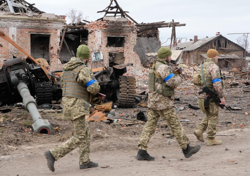 Quân đội Ukraine tái chiếm lại thị trấn Trostyanets hôm 26/3. Ảnh: những binh sĩ Ukraine đi ngang qua xác một chiếc xe tăng Nga giữa đống đổ nát (Ảnh: AP).