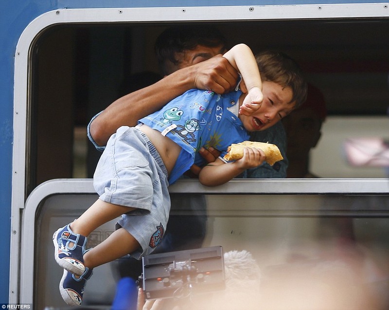 Một chú bé đang được cố kéo qua cửa sổ để lên con tàu chật ních những người chạy nạn đói khát và tuyệt vọng