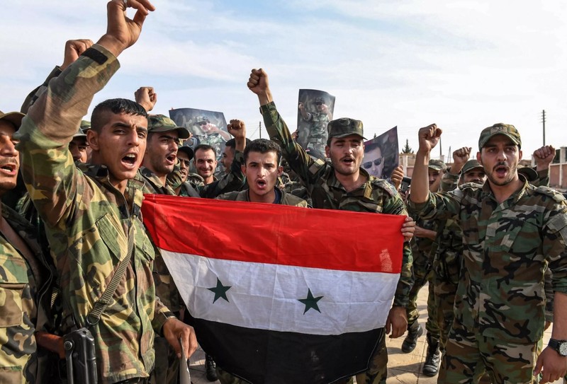 Quân đội chính phủ Syria giơ cao quốc kỳ và ảnh Tổng thống Assad tại ngoại ô thành phố Manbij hôm 15/10 (Ảnh: Newsweek)