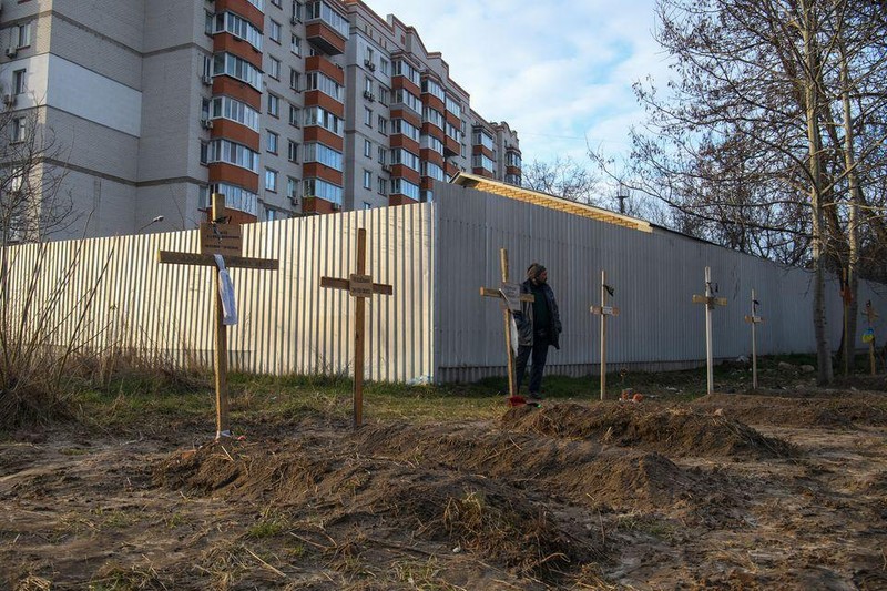 Một người đàn ông đứng bên cạnh những ngôi mộ ở Bucha Ukraine (Ảnh: Reuters)