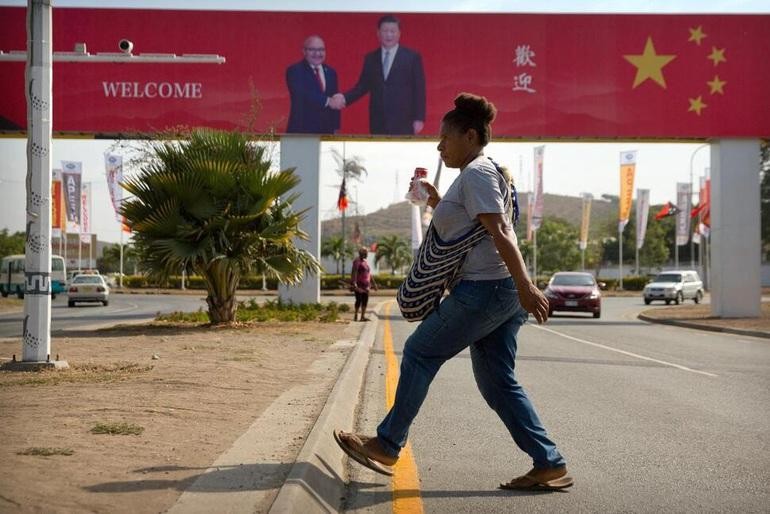 Một phụ nữ bước qua con đường, nơi có áp phích chào đón chuyến thăm của Chủ tịch Trung Quốc Tập Cận Bình ở Papua New Guinea năm 2018 (Ảnh: AP).
