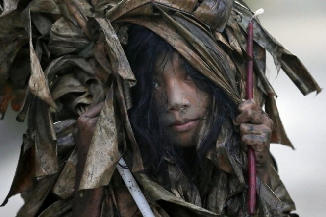 Một bé gái quàng lá chuối khô và trét bùn lên cơ thể trong lúc diễn ra lễ hội người bùn - Ảnh: AP