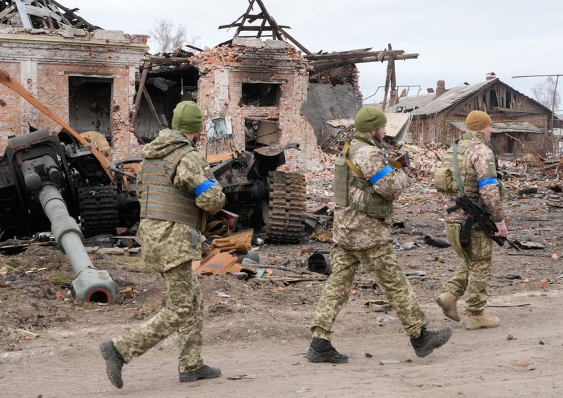 Quân đội Ukraine tái chiếm lại thị trấn Trostyanets hôm 26/3. Ảnh: những binh sĩ Ukraine đi ngang qua xác một chiếc xe tăng Nga giữa đống đổ nát (Ảnh: AP).