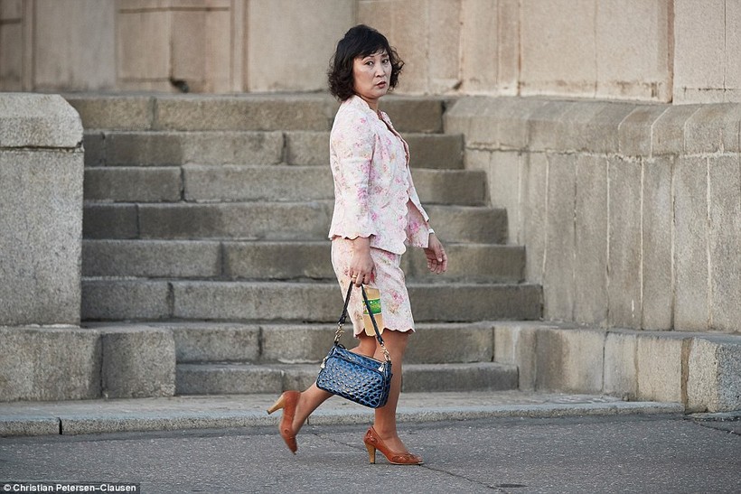 Một phụ nữ ăn mặc thời trang, tay cầm túi xách da cá sấu, chân đi giày cao gót đang dạo bộ trên đường phố Bình Nhưỡng - Triều Tiên.