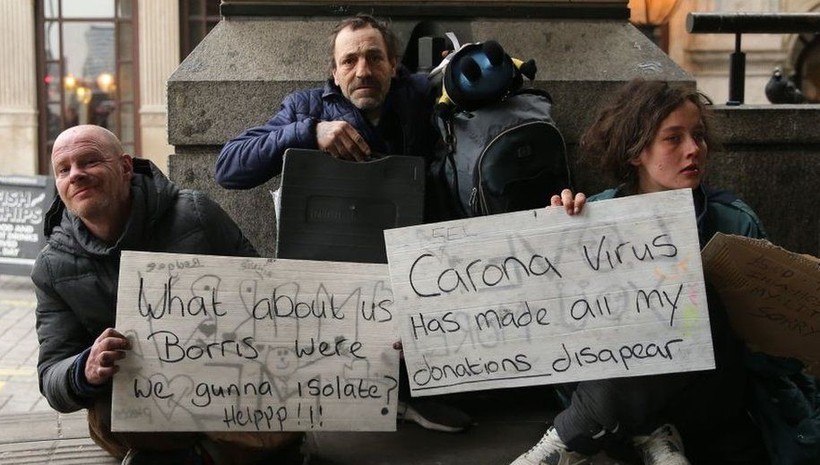 Người vô gia cư tại Luân Đôn (Anh) đang cầm tấm bảng với các thông điệp “Chúng tôi thì sao, Boris (Thủ tướng Anh)? Chúng tôi sẽ được cách ly chứ? Làm ơn giúp!”, “Virus Corona làm biến mất mọi thu nhập của tôi” - Ảnh: BBC.