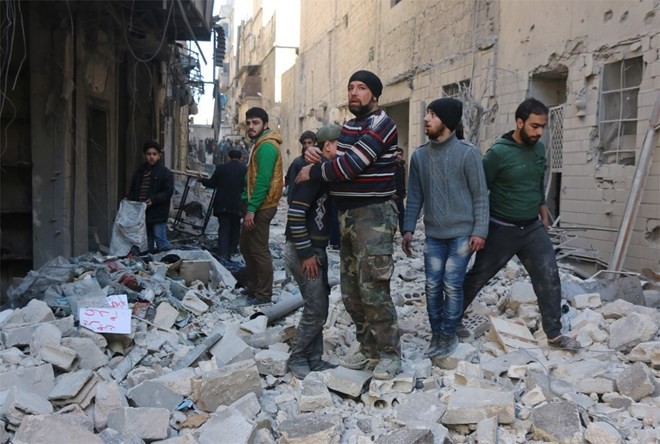 Người dân Syria đứng cạnh một tòa nhà bị hủy hoại ở thành phố Aleppo.